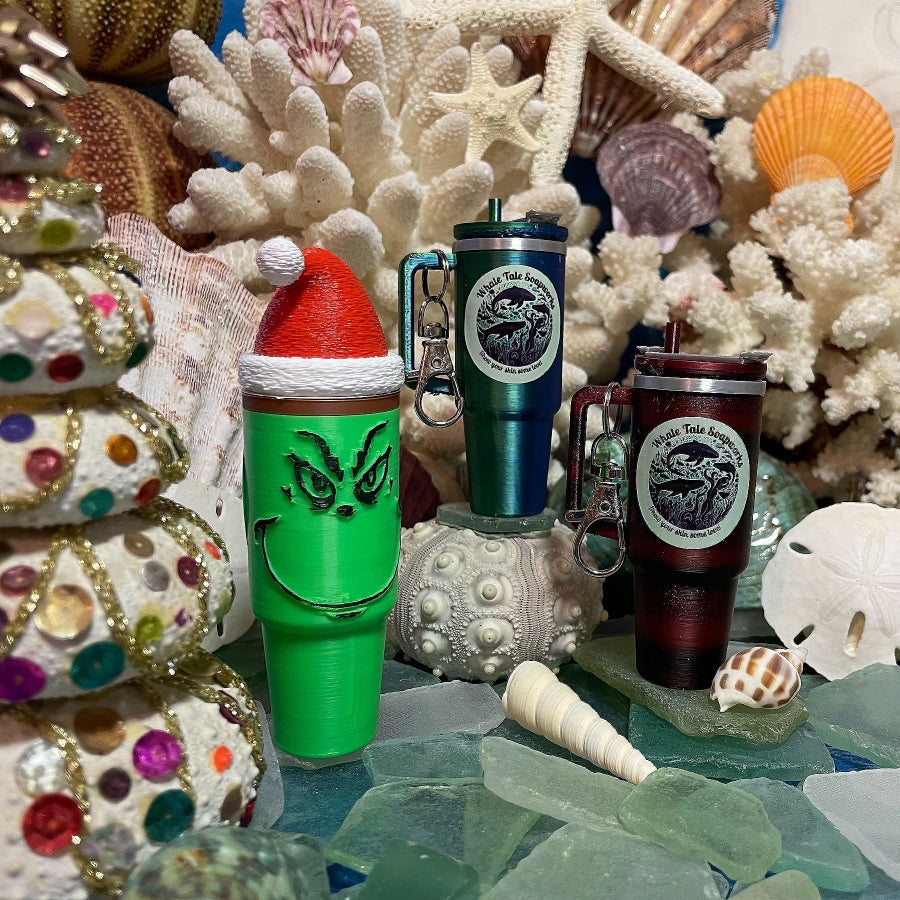 Three Mini Tumbler Lip Balm Keychains. Colors include festive lime green with a Santa hat, color-changing blue and green, and stacked red and black—each featuring the Whale Tale Soapworks logo.